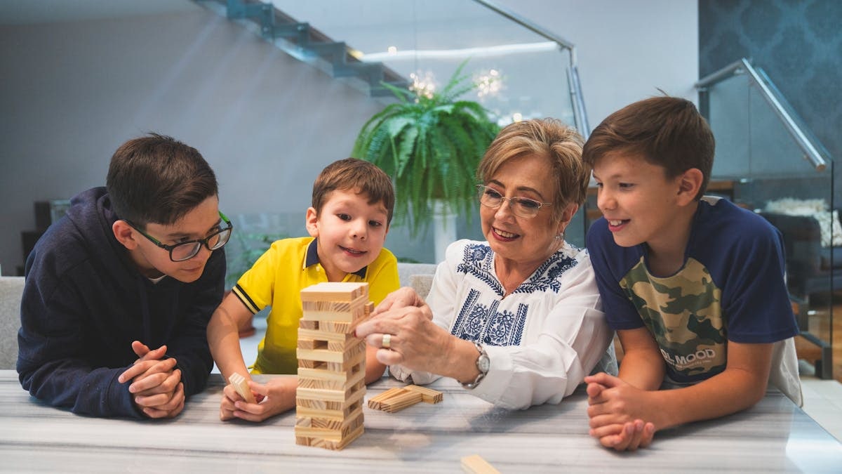 A joyful family moment with grandma and grandsons playing Jenga indoors, capturing quality time together.
