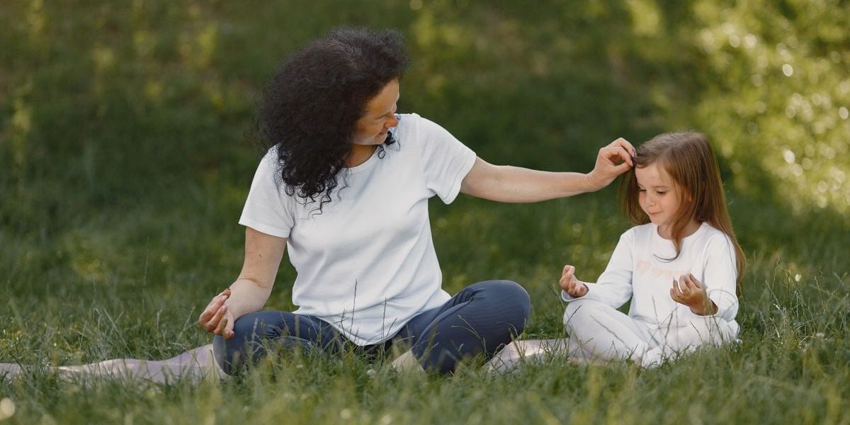 Mother and daughter bonding through yoga outdoors in a serene grassy field.