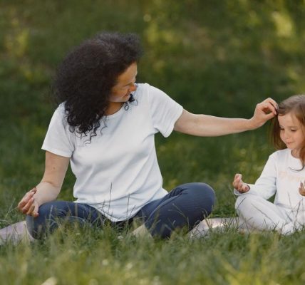 Mother and daughter bonding through yoga outdoors in a serene grassy field.