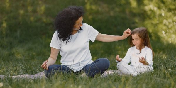 Mother and daughter bonding through yoga outdoors in a serene grassy field.