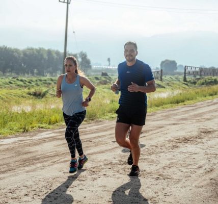 Active couple jogging on a dirt road in a scenic rural area under the bright sun.