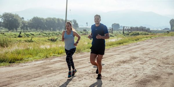 Active couple jogging on a dirt road in a scenic rural area under the bright sun.